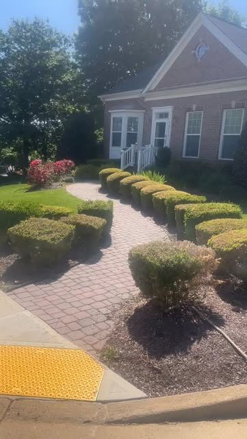 A brick front walkway lined with trimmed shrubs and fresh mulch