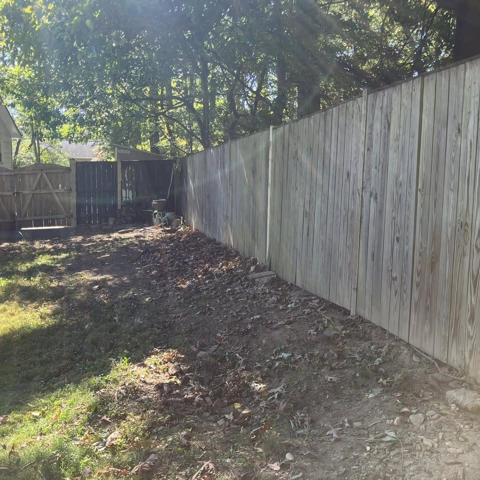 A cleared and graded strip of bare soil along a wood privacy fence
