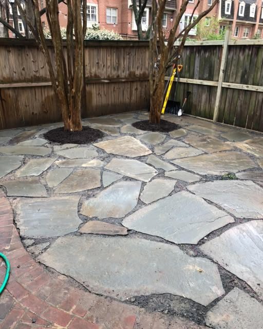 A finished flagstone patio set between two trees in a fenced backyard